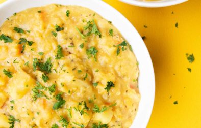 two bowls of cheesy red lentil soup on a yellow background with parsley on top