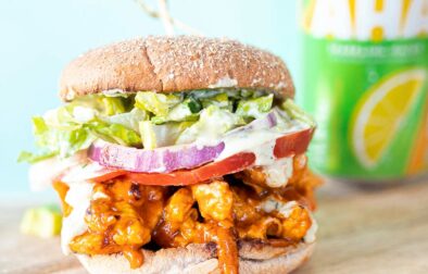 a vegan buffalo chicken sandwich on a wooden slab with a seltzer in the background