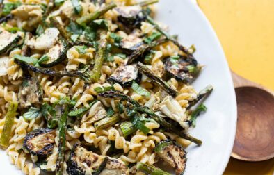 grilled vegetable pasta salad on a large serving plate with a cloth napkin and wooden tongs